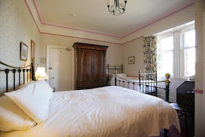 A bedroom with a large bed, a wooden wardrobe, a desk, and a window with curtains.