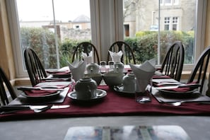 A dining table set for four with white tableware and a red tablecloth, positioned near a window with a view of buildings and greenery.