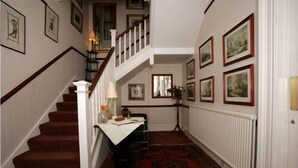 A hallway with a staircase, a radiator, and framed pictures on the walls. - Bellevue Guest House (Kelso)