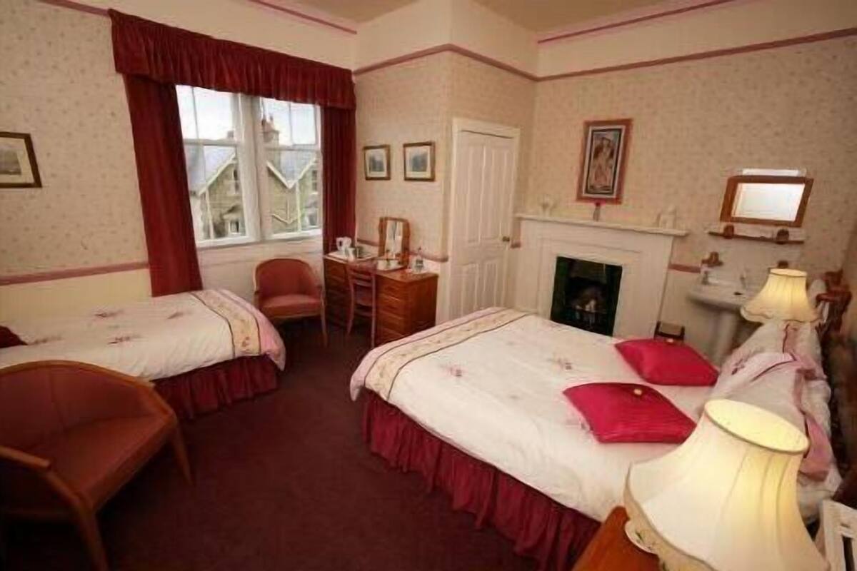 Een hotelkamer met twee bedden, een bureau, een stoel, een open haard en een raam met gordijnen.