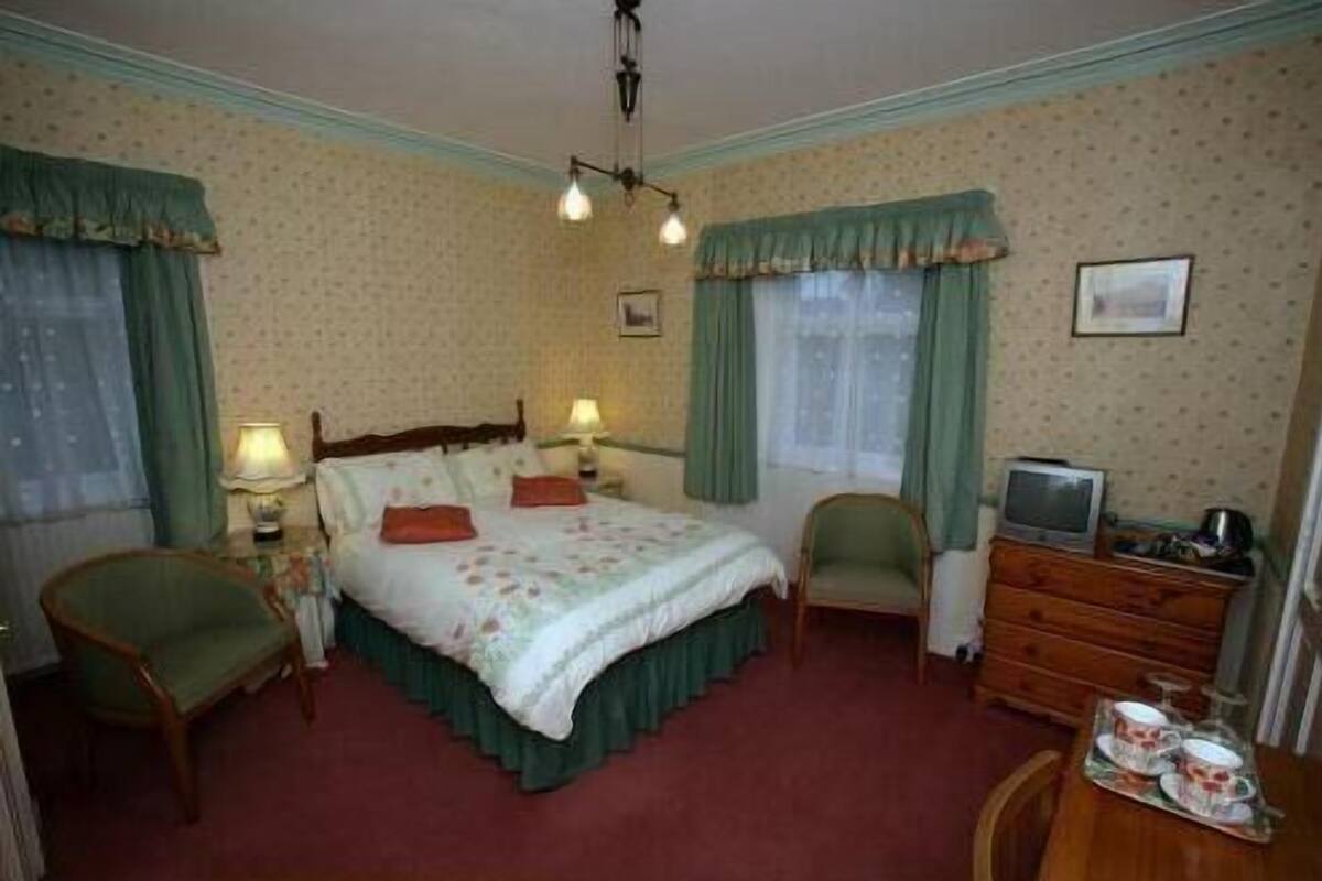 Hotelkamer met een bed, twee stoelen, een dressoir, een televisie en een raam met gordijnen.