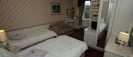 Quarto de hotel com duas camas de solteiro, uma escrivaninha, uma cadeira, um guarda-roupa e um espelho.