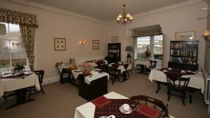 A dining area with multiple tables, chairs, and a chandelier. There are bookshelves and a window with curtains. - Bellevue Guest House (Kelso)