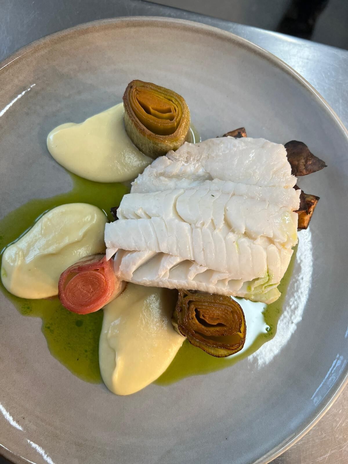 Un plato con pescado blanco, verduras asadas y salsa cremosa.