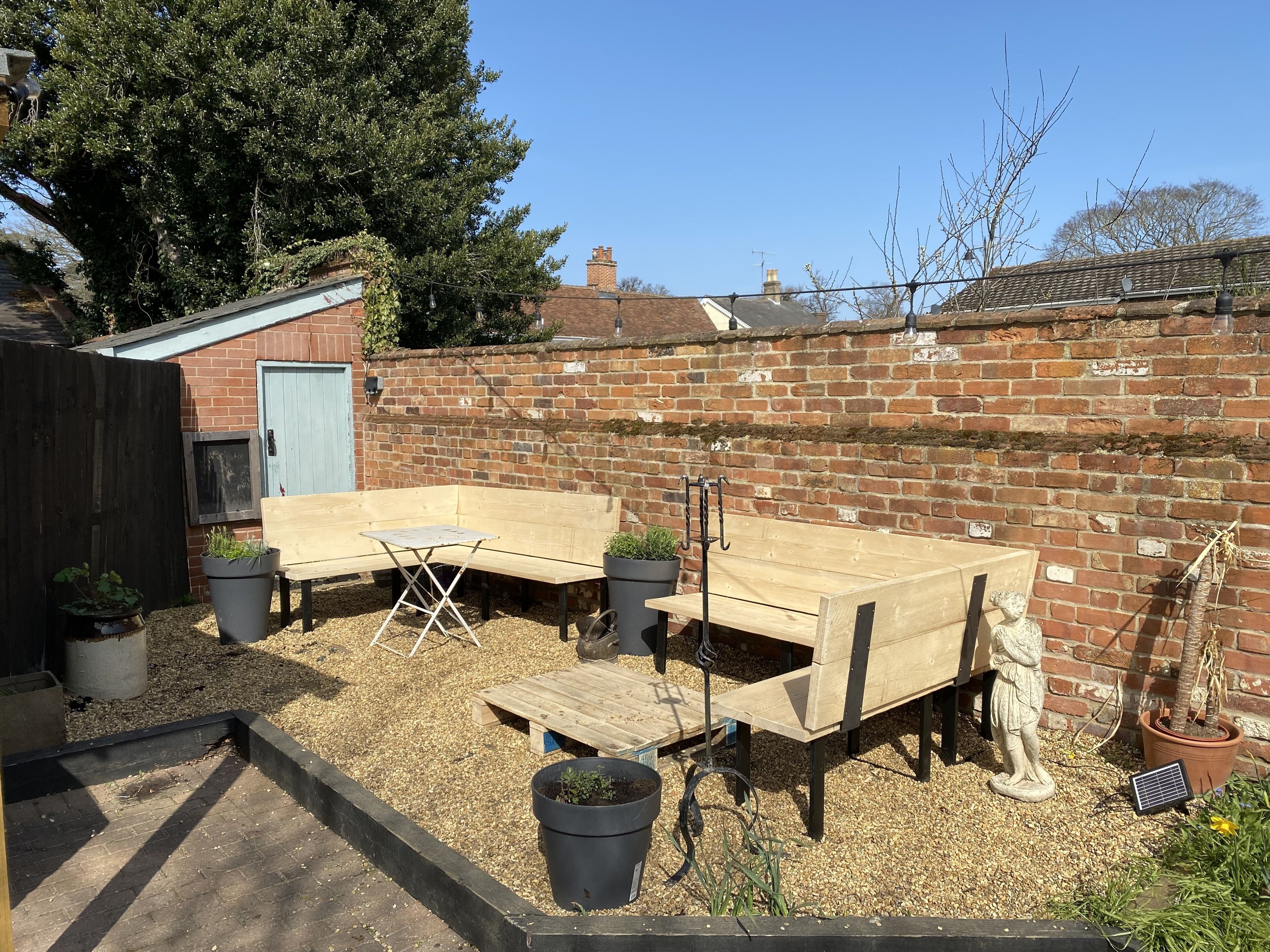 A backyard with a wooden bench, a small table, and potted plants.