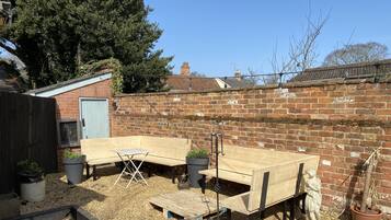 A backyard with a wooden bench, a small table, and potted plants.