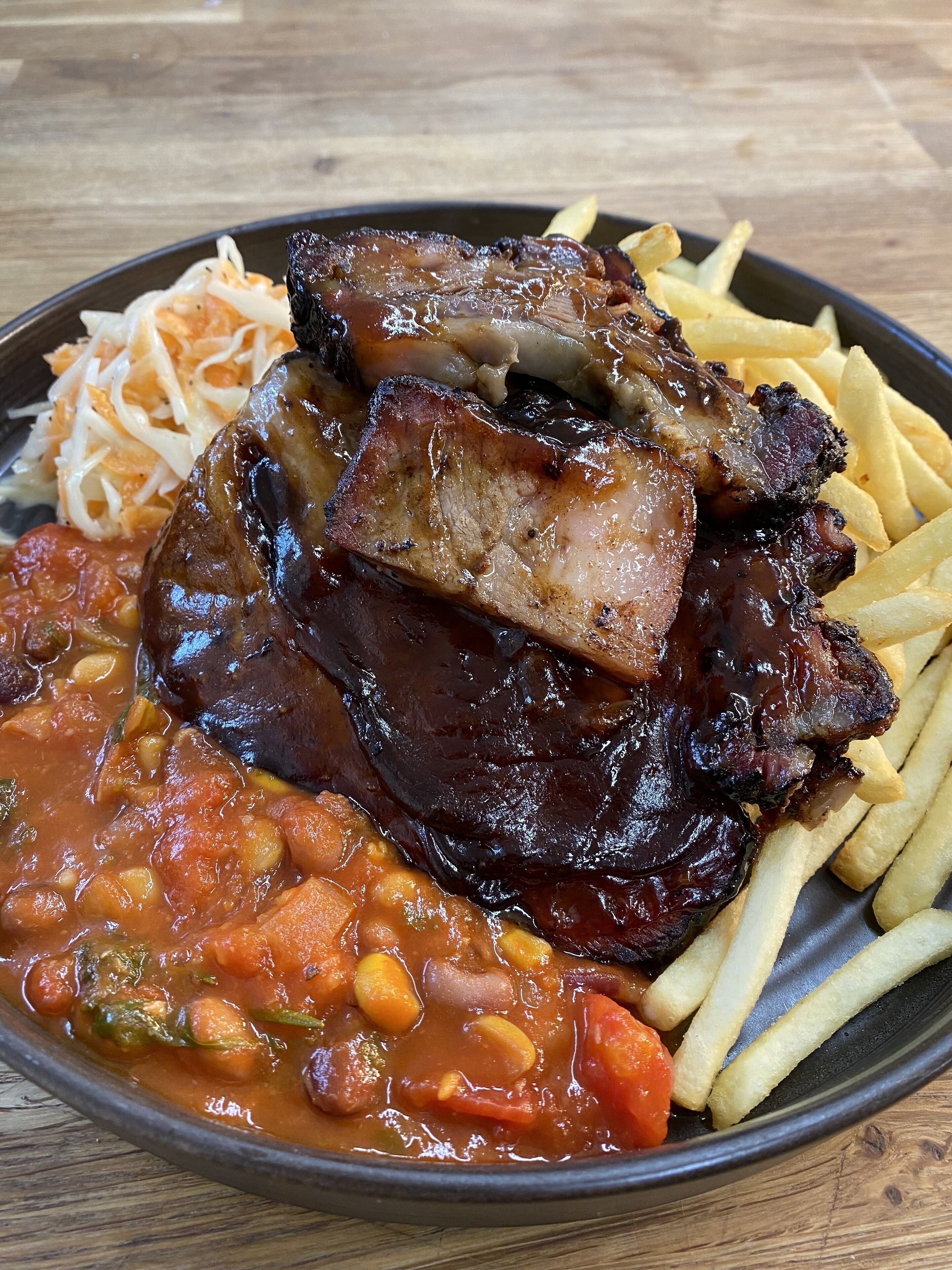 Prato de comida com costelas, batatas fritas e feijão.