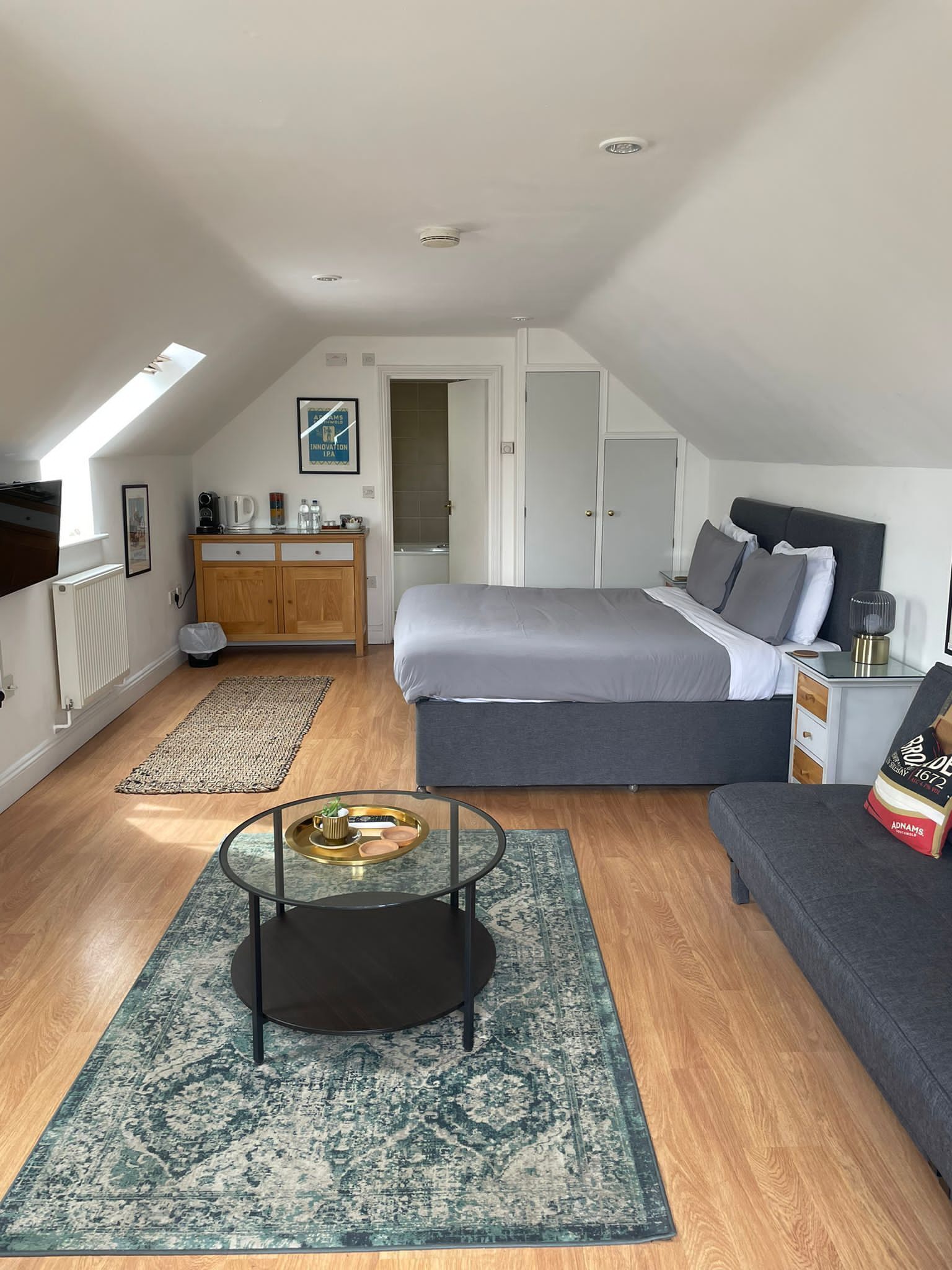Een moderne loft slaapkamer met dakraam, groot bed, een bank, een tafeltje en een kast.