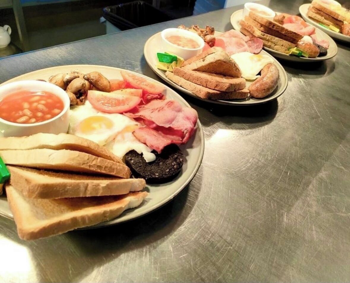 Una mesa de acero inoxidable con platos de comida para el desayuno, incluyendo tostadas, huevos, tocino y frijoles.