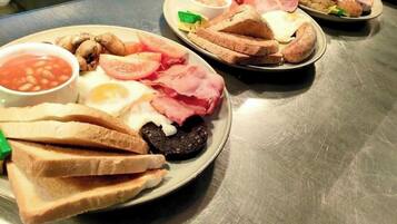 Una mesa de acero inoxidable con platos de comida para el desayuno, incluyendo tostadas, huevos, tocino y frijoles.