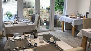 Comedor con mesas dispuestas para dos, con vistas a un jardín a través de amplias ventanas.
