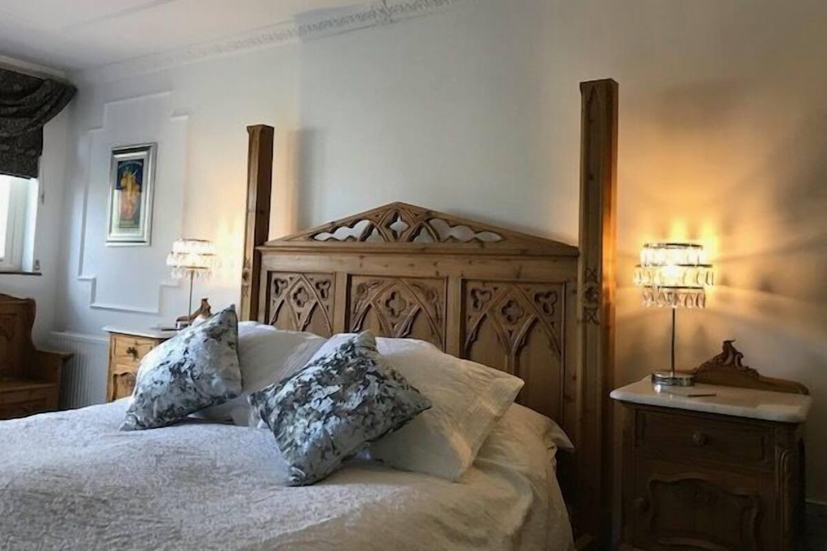 Un lit bien fait, avec une tête de lit en bois, deux tables de chevet avec des lampes et un tableau encadré au mur.