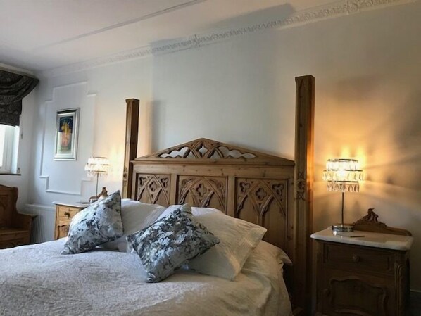 Una cama bien hecha con cabecera de madera, dos mesitas de noche con lámparas y un cuadro enmarcado en la pared.