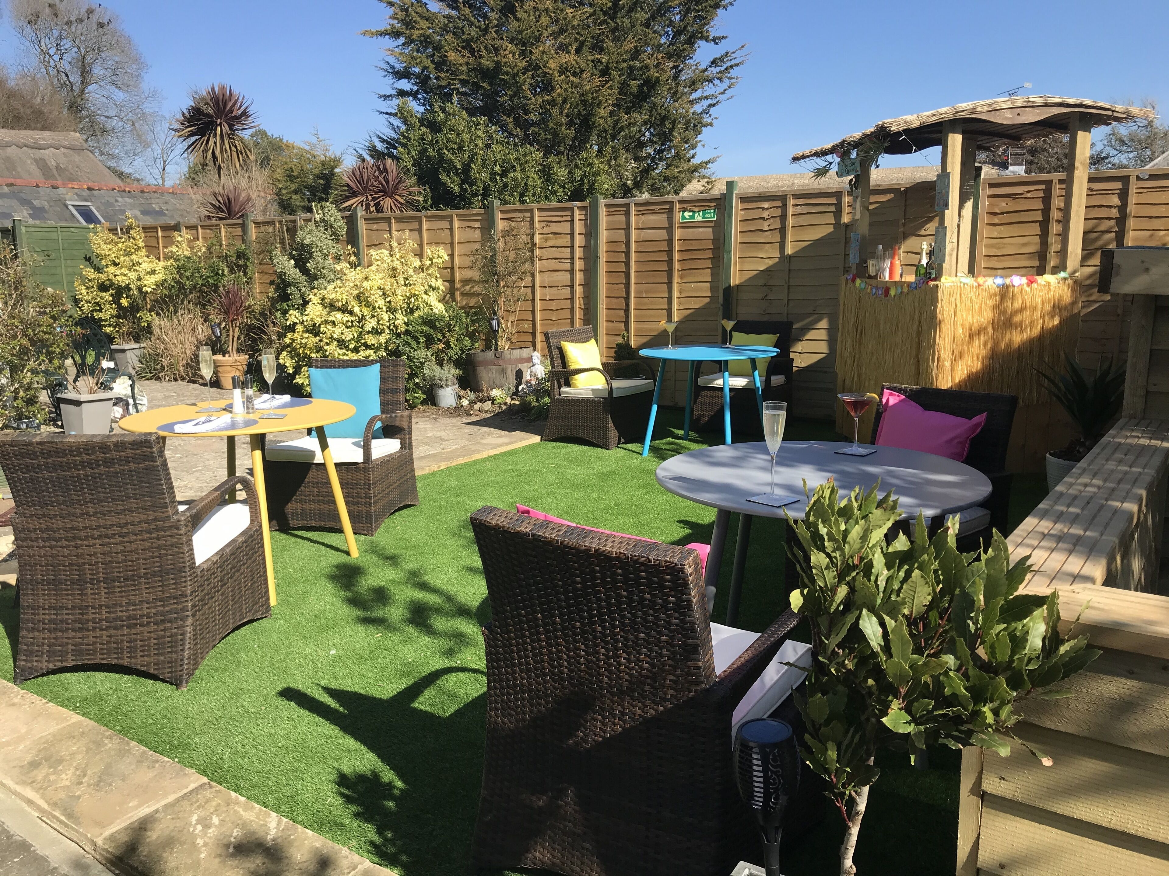 An outdoor patio with wicker furniture, artificial grass, and a wooden fence.