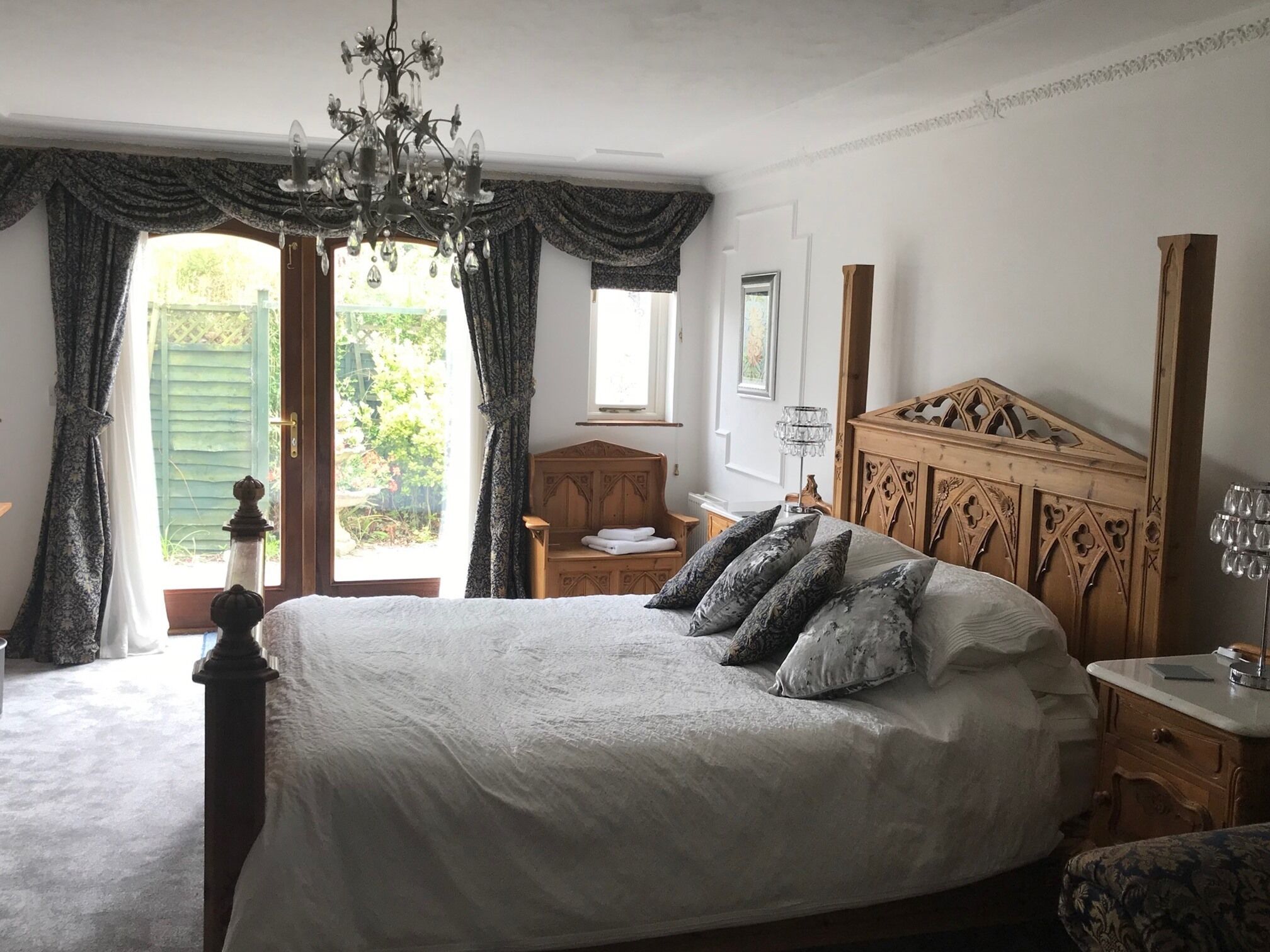 Een slaapkamer met een groot bed, een houten hoofdeinde, een kroonluchter en uitzicht op de omgeving.