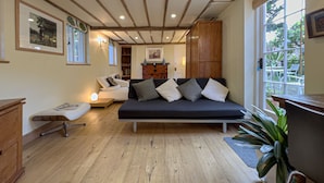 Een gezellige woonkamer met een donkere bank, houten vloeren en een groot raam met uitzicht op het landschap.