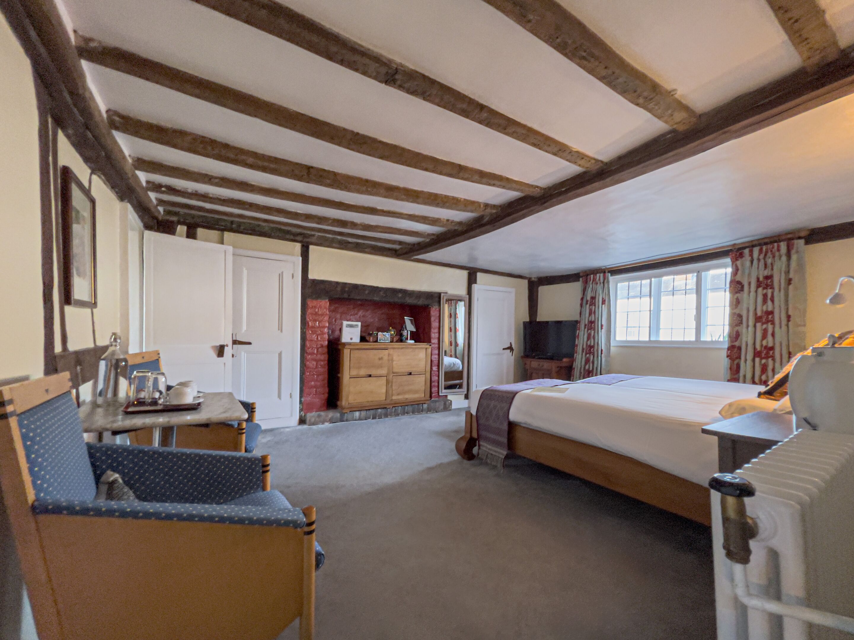 A cozy room with a bed, a wooden cabinet, a television, and a window with curtains.