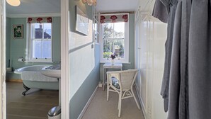 Een badkamer met een badkuip, een raam met uitzicht, een rieten stoel en een badjas aan een rek.