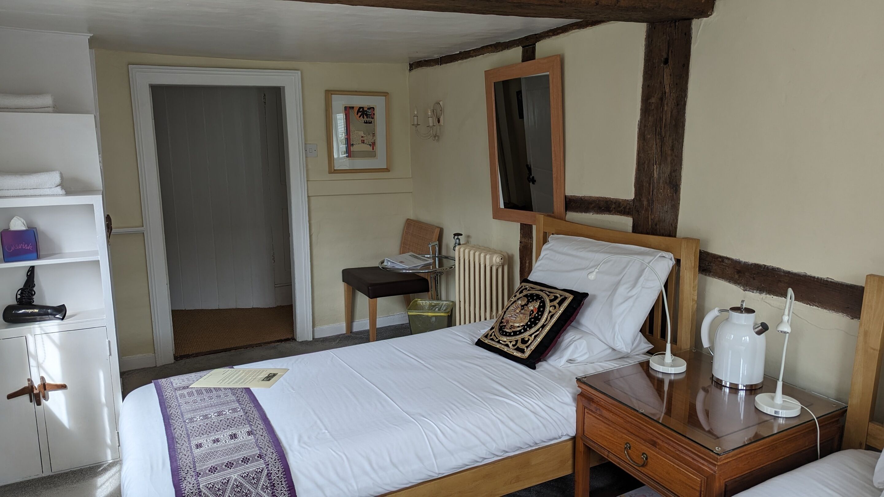 A neatly arranged hotel room with a bed, bedside table, and a small desk with a chair.
