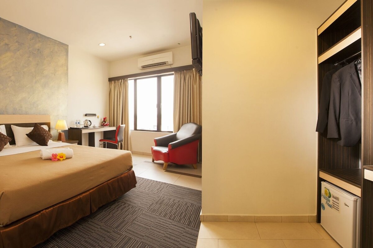 A hotel room with a large bed, a desk, a chair, a TV, and a wardrobe.