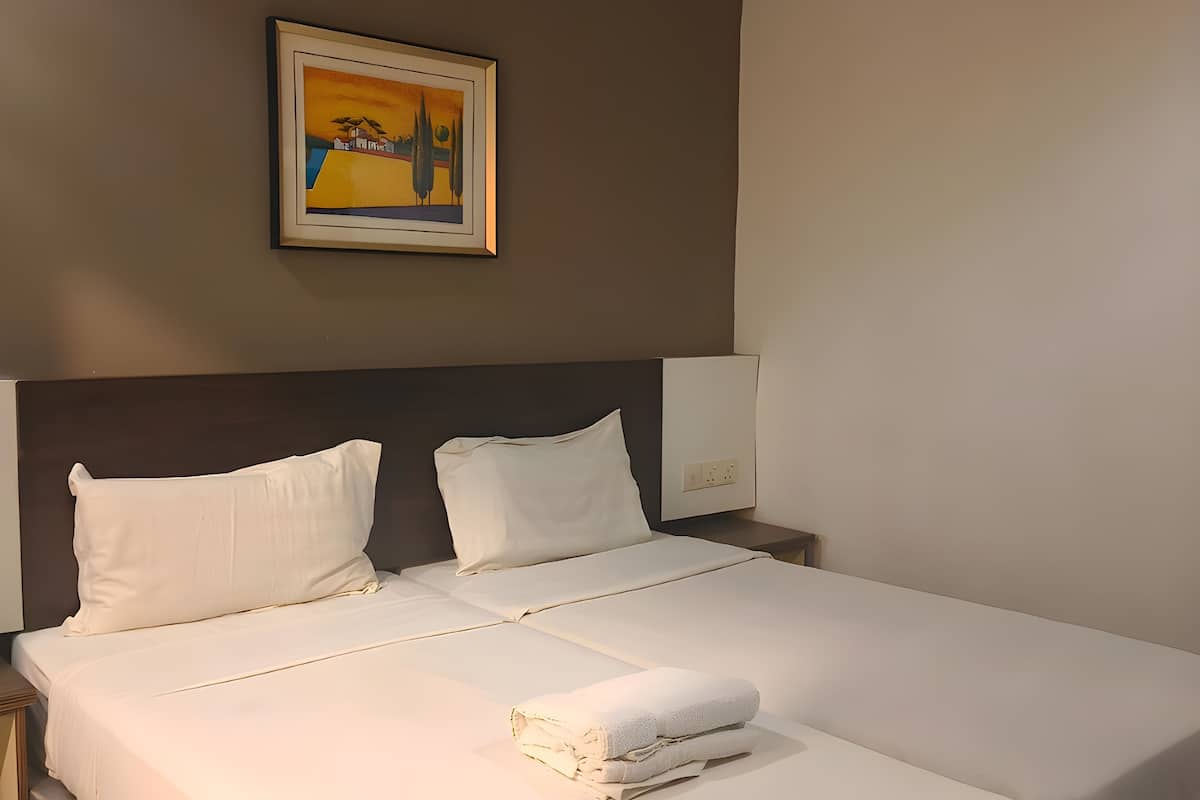 A neatly made bed with white linens, a headboard, and a painting above it.