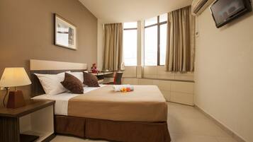 Une chambre d’hôtel avec un lit, un bureau, une chaise, une télévision et une fenêtre avec des rideaux.