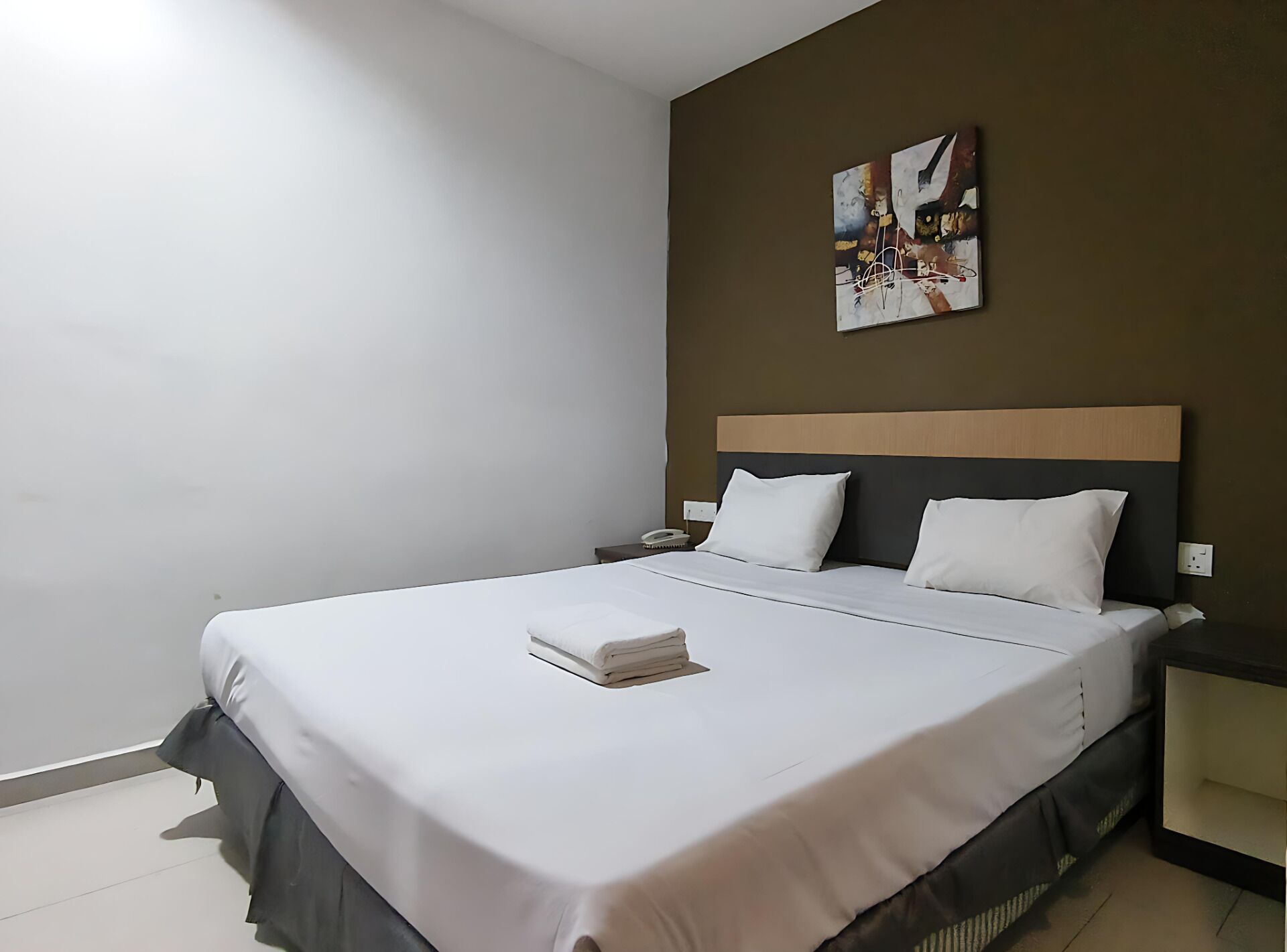 Een hotelkamer met een groot bed, een nachtkastje, een aan de muur hangend kunstwerk en een effen muur.