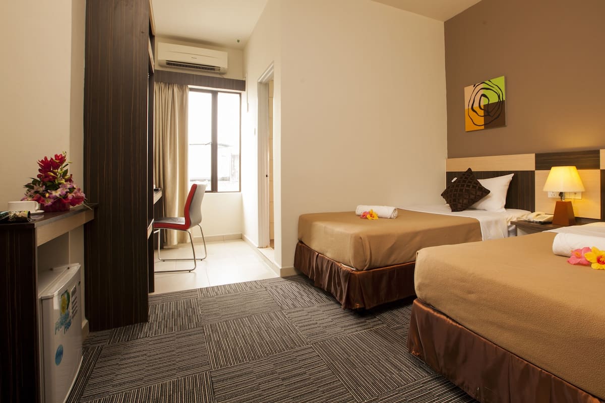 A hotel room with two beds, a desk, a chair, and a window with curtains.