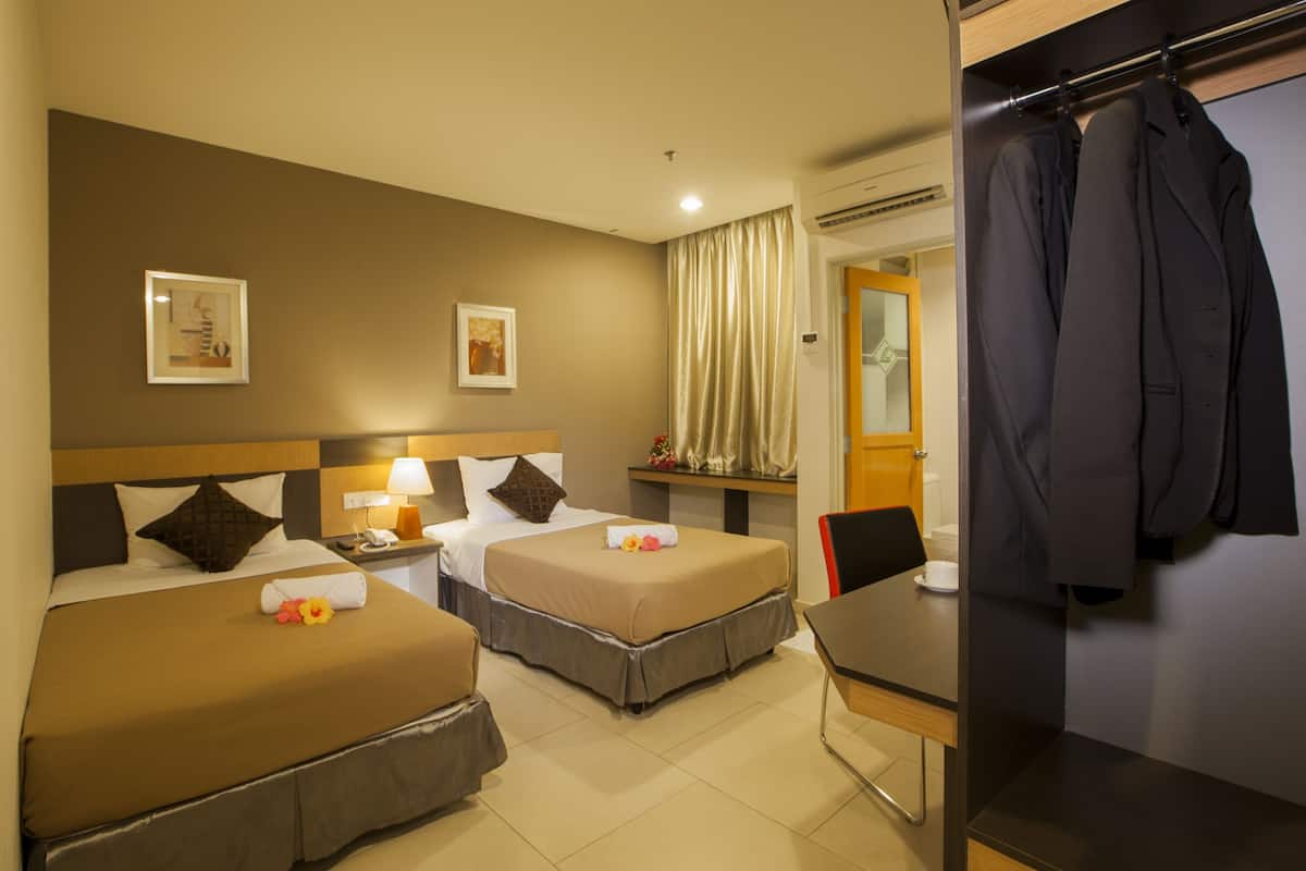 A hotel room with two beds, a desk, and a chair. There is a coat rack with a jacket hanging on it.