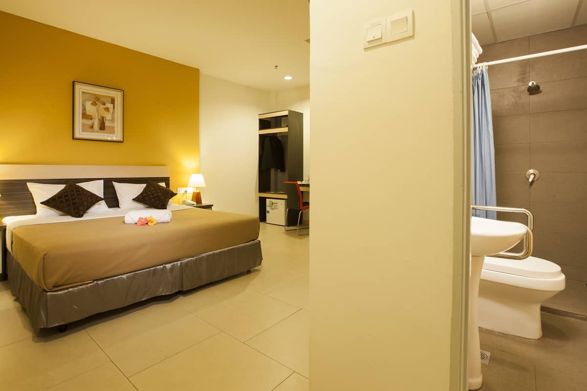 A hotel room with a neatly made bed, a desk with a chair, a bathroom with a toilet and shower, and a framed picture on the wall.