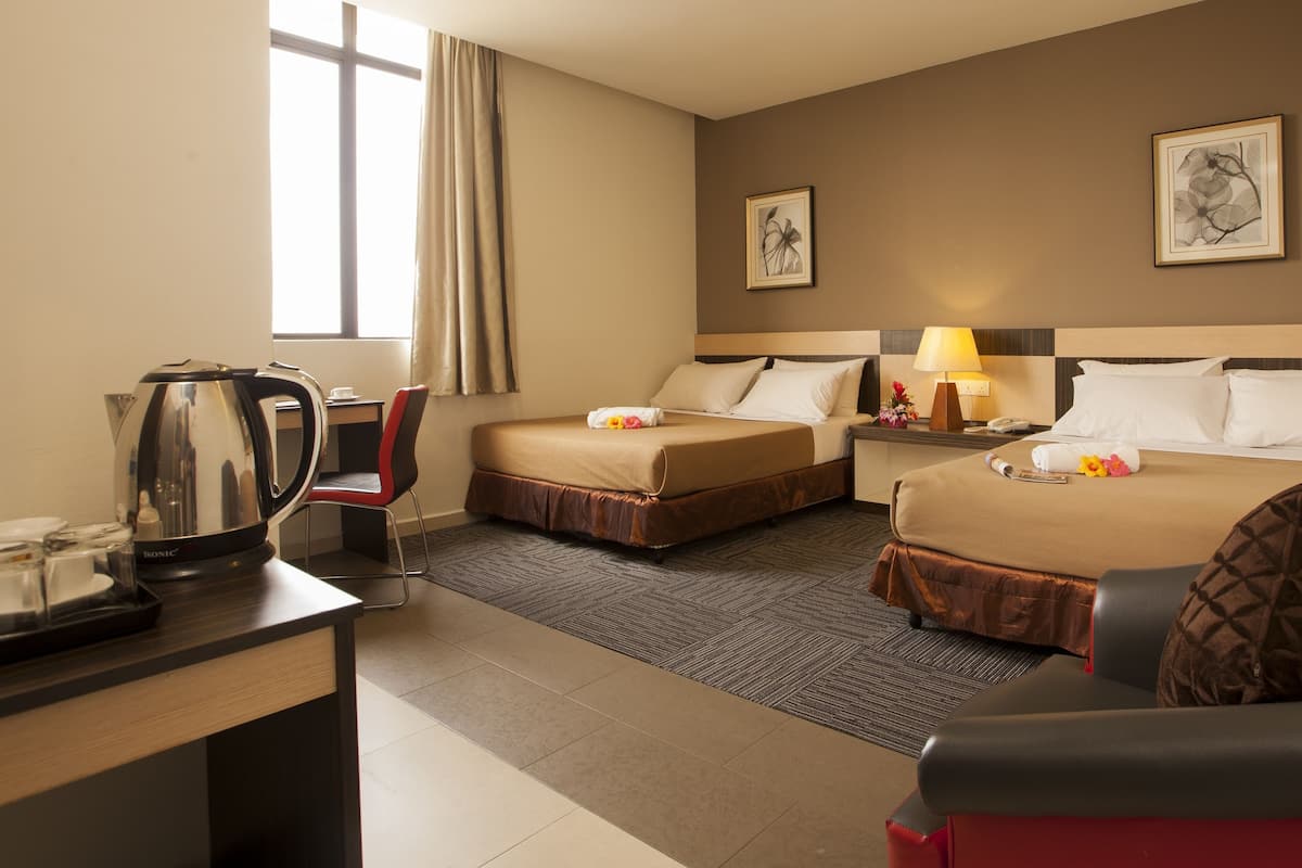 A hotel room with two beds, a desk with a kettle, a chair, a lamp, and two framed pictures on the wall.