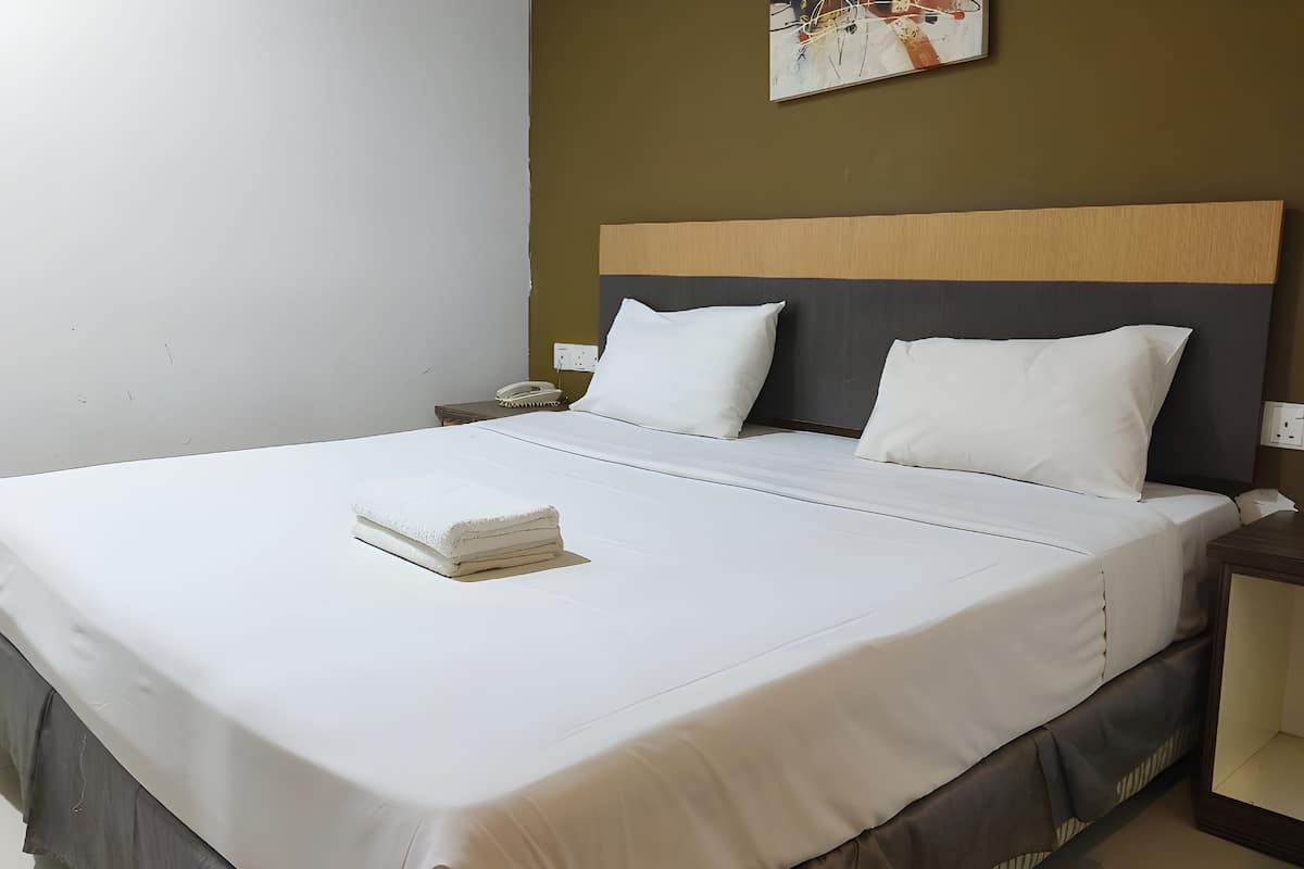 A neatly made bed with white linens, a wooden headboard, and a small bedside table with a telephone.