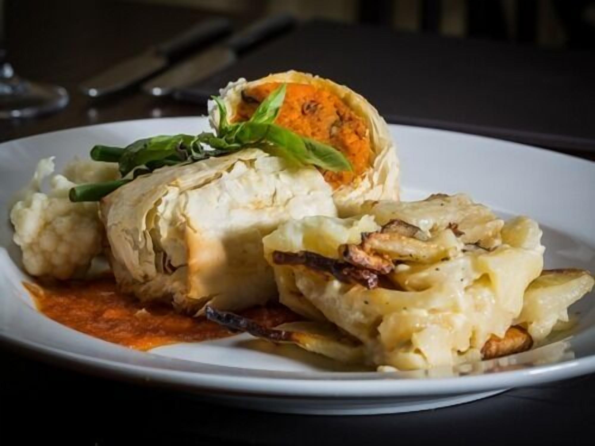 Un plato de comida con un pastel relleno, puré de papas y salsa.