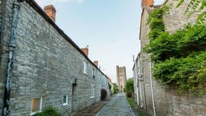 A narrow cobblestone street flanked by stone buildings with small windows and a tower in the distance. - Mildmay Arms (Yeovil)