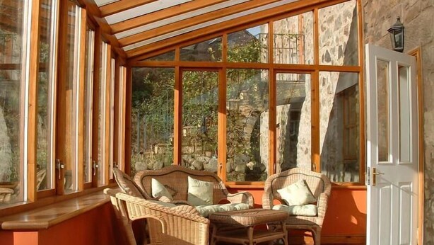 A sunroom with wicker furniture, large windows, and a stone wall.