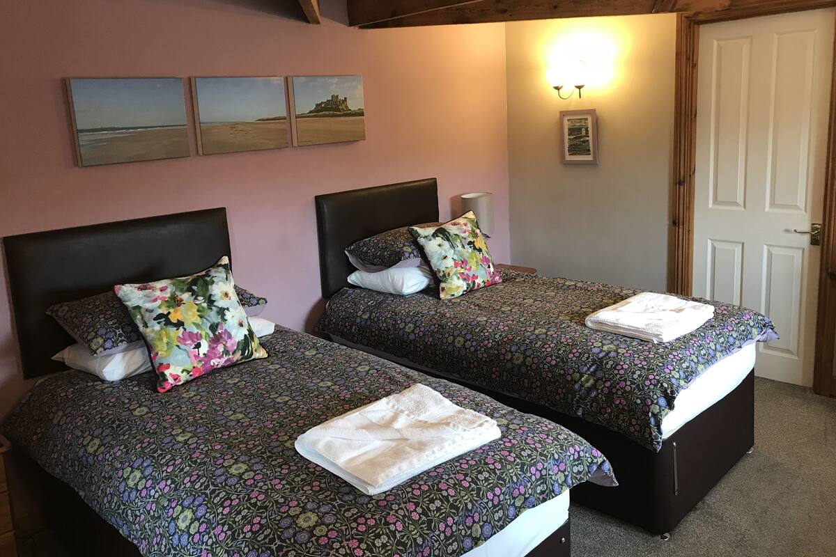 Duas camas de solteiro com roupa de cama floral, teto de madeira e um quadro pendurado na parede com um castelo.