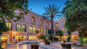 A courtyard with outdoor seating, palm trees, and a building with arched windows. - El Ksar Resort & Spa (Sousse)
