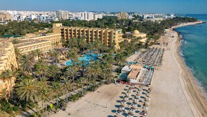 Oversigtsbillede af et strandresort med flere hotelbygninger, et stort poolområde og mange strandparasoller.