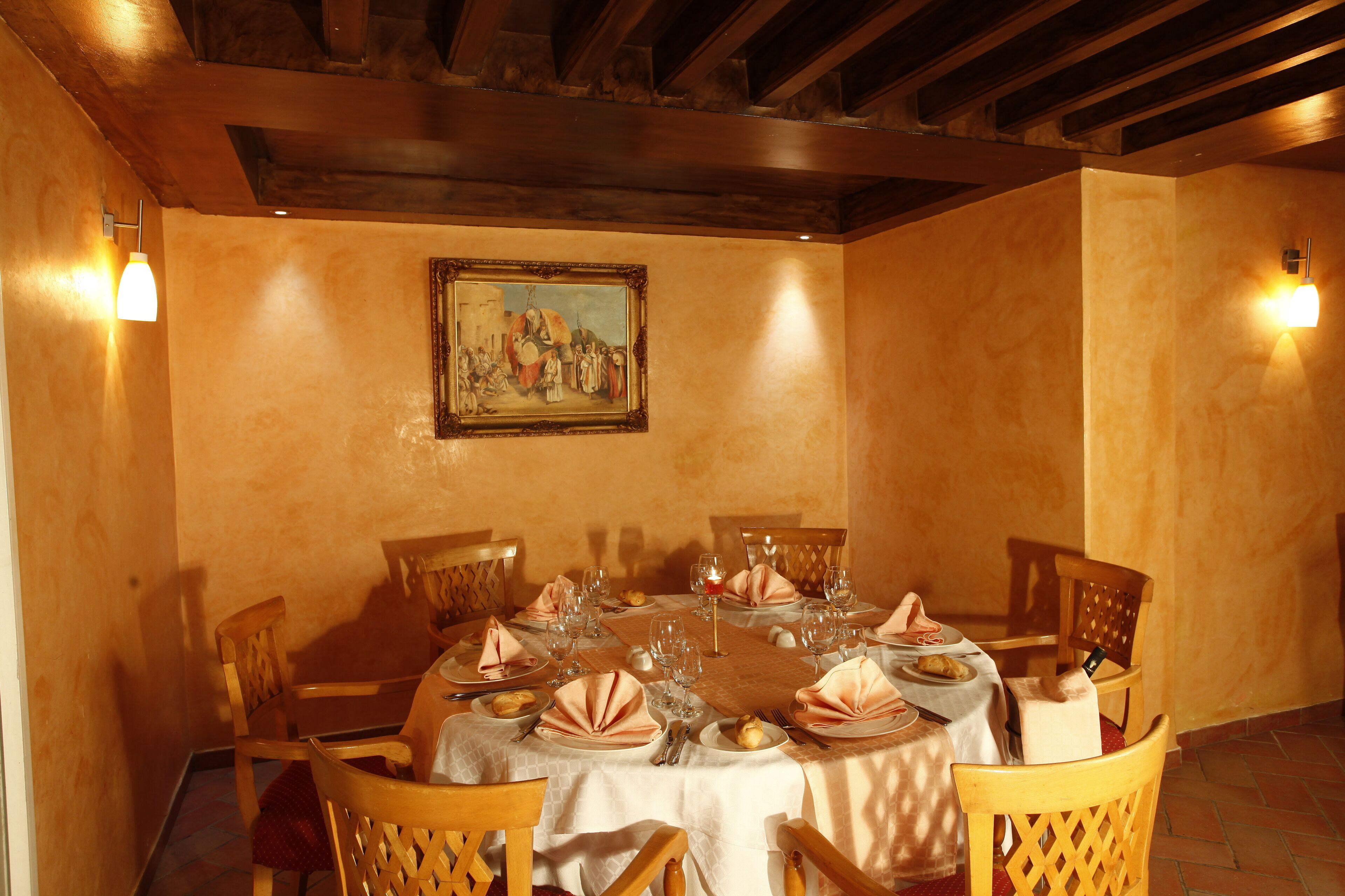 Comedor con una mesa redonda dispuesta para cuatro personas, sillas de madera, un cuadro en la pared y dos luces fijadas a la pared.