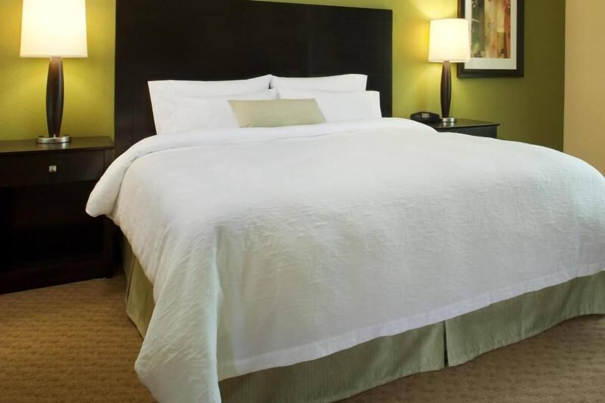 A neatly made bed with white linens, two bedside lamps, and a dark headboard.