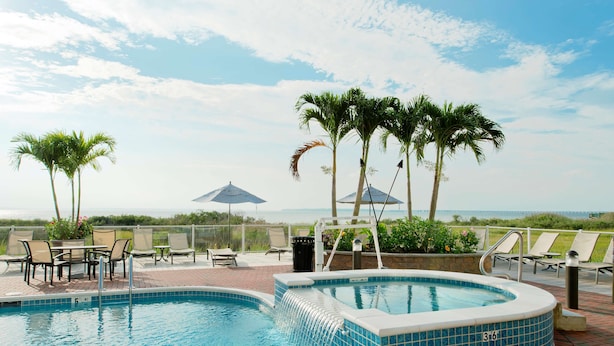 A pool area with lounge chairs, a hot tub, and a view of the ocean.