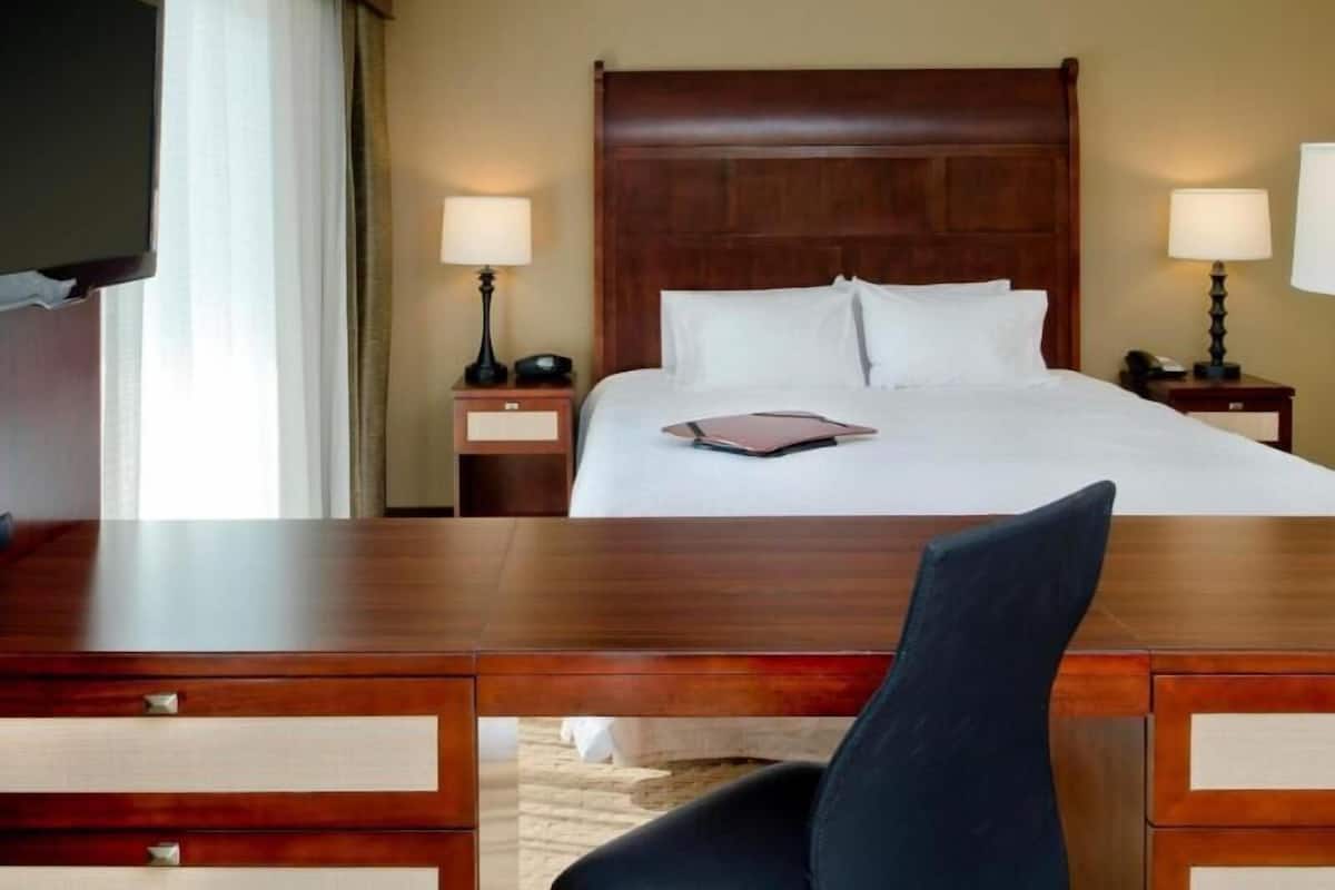 A hotel room with a large bed, two bedside tables with lamps, a desk with drawers, and a television.