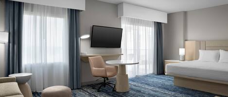 Ein Hotelzimmer mit Bett, Schreibtisch, Stuhl, Fernseher und einem großen Fenster mit Vorhängen.