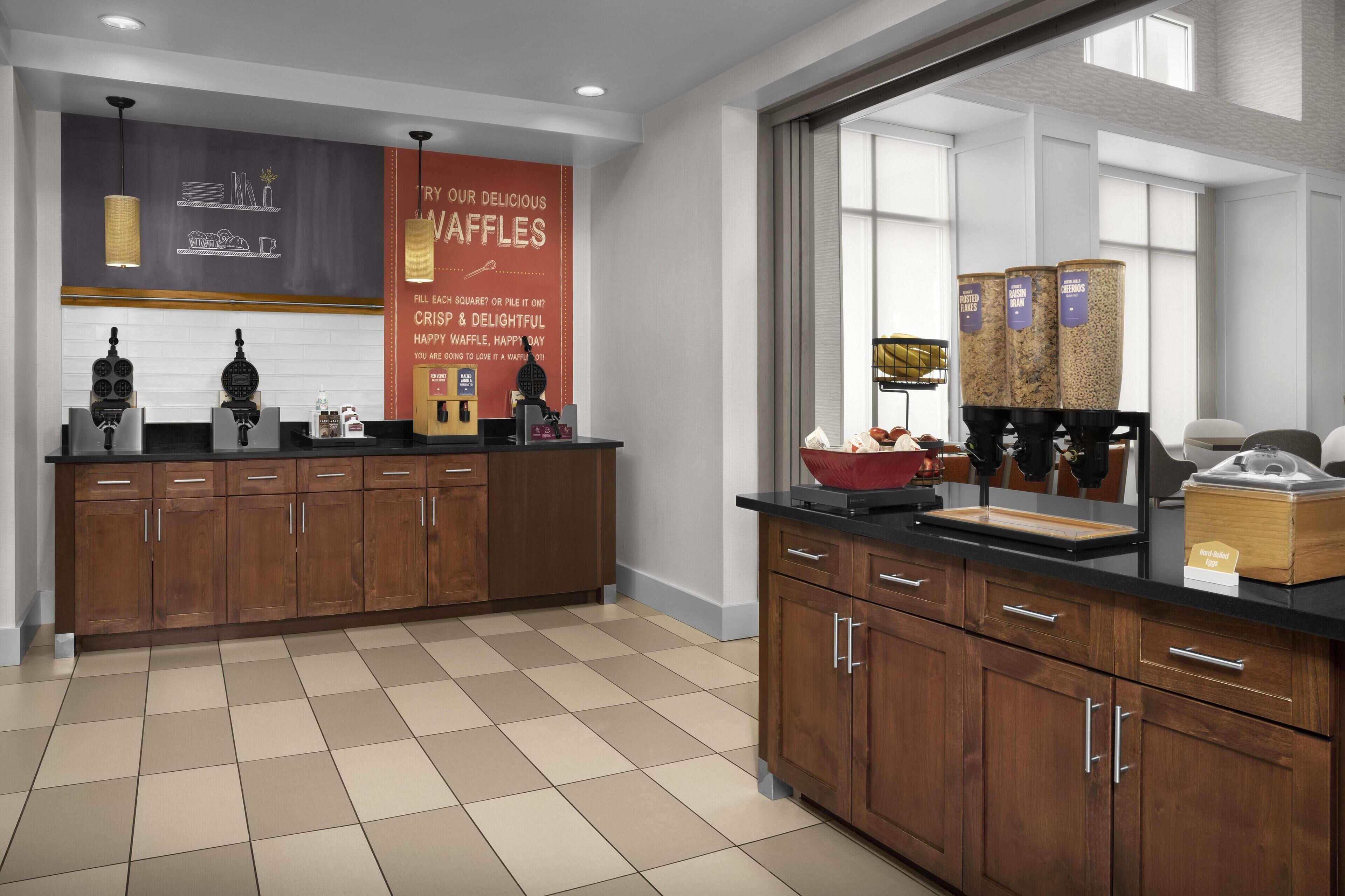 A modern kitchen with wooden cabinets, a black countertop, and waffle-making equipment.