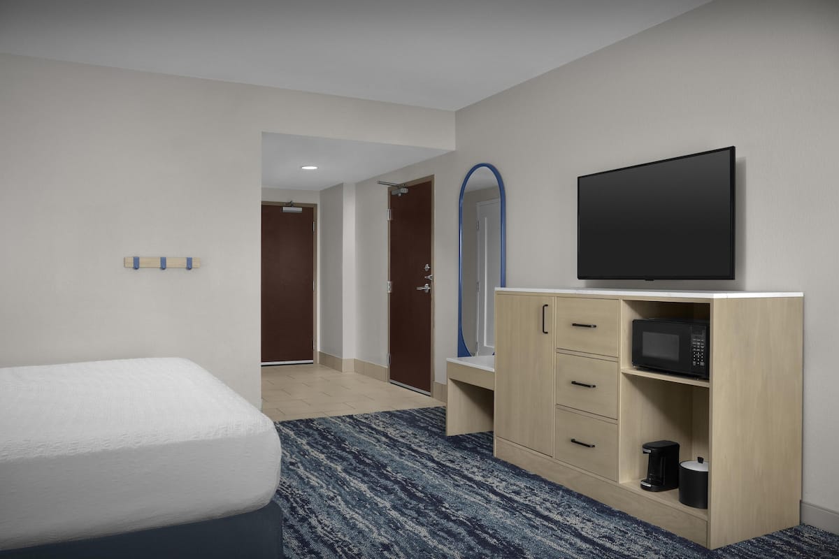 A hotel room with a bed, a TV, a microwave, and a cabinet.