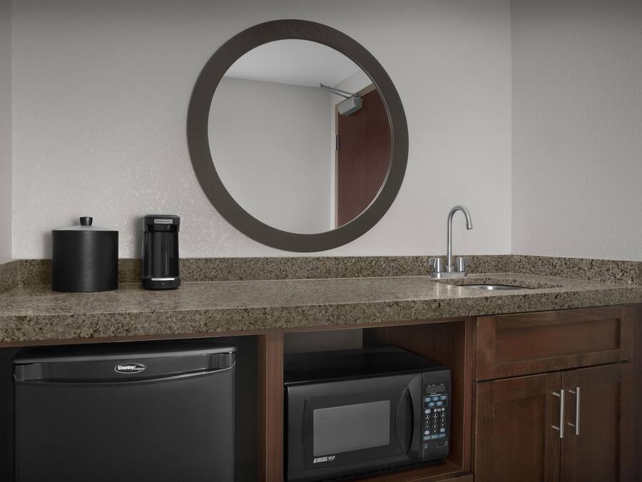 A modern bathroom with a granite countertop, a black coffee maker, a sink with a faucet, a microwave, and a Danby Designer dishwasher.