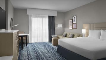 A hotel room with a large bed, a desk, a chair, a sofa, and a TV.