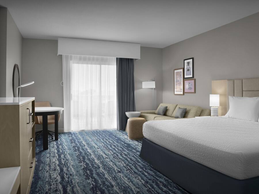 A hotel room with a large bed, a desk, a chair, a sofa, and a TV.