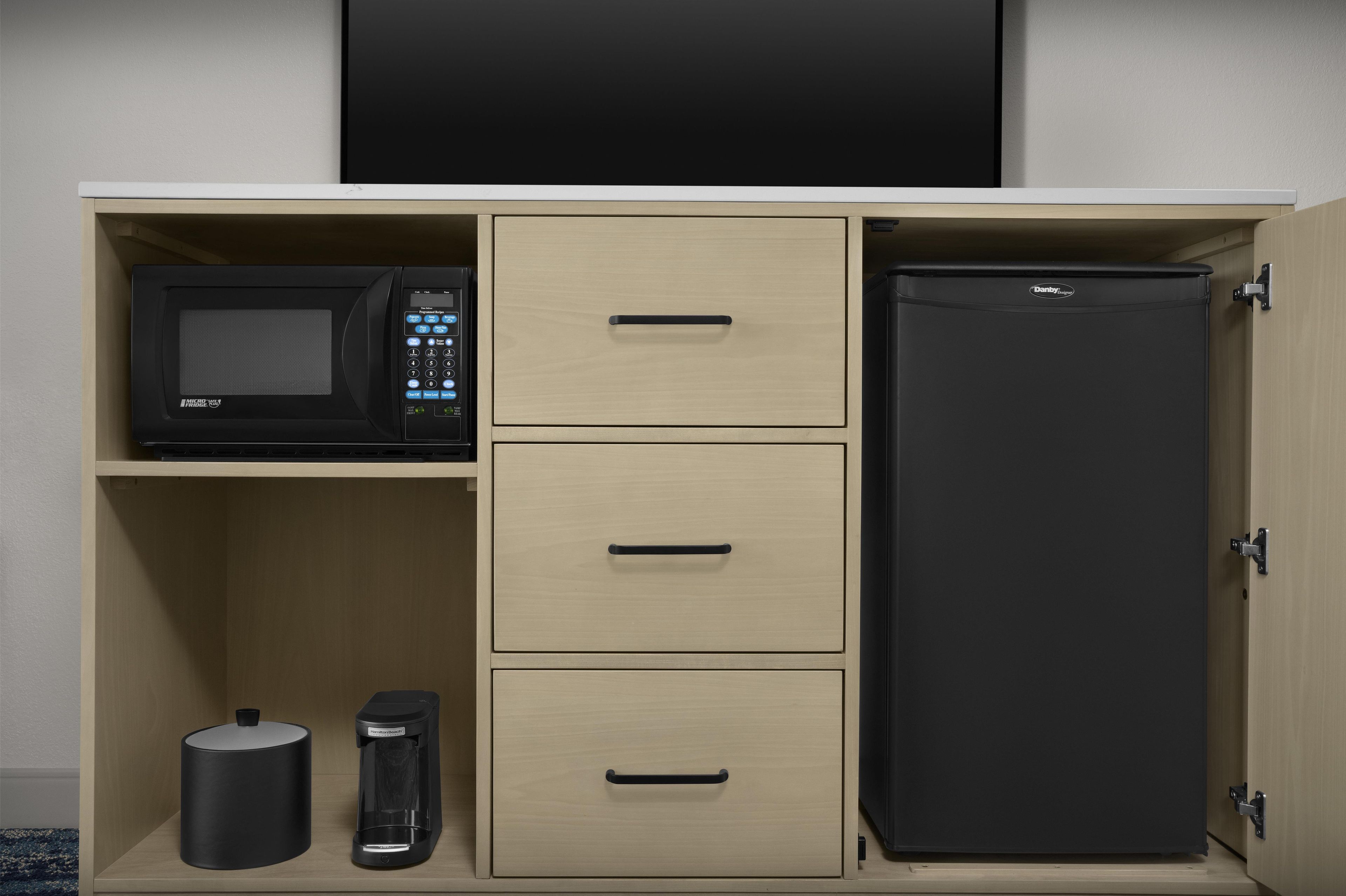 Una cocina equipada con microondas, refrigerador y tres cajones.