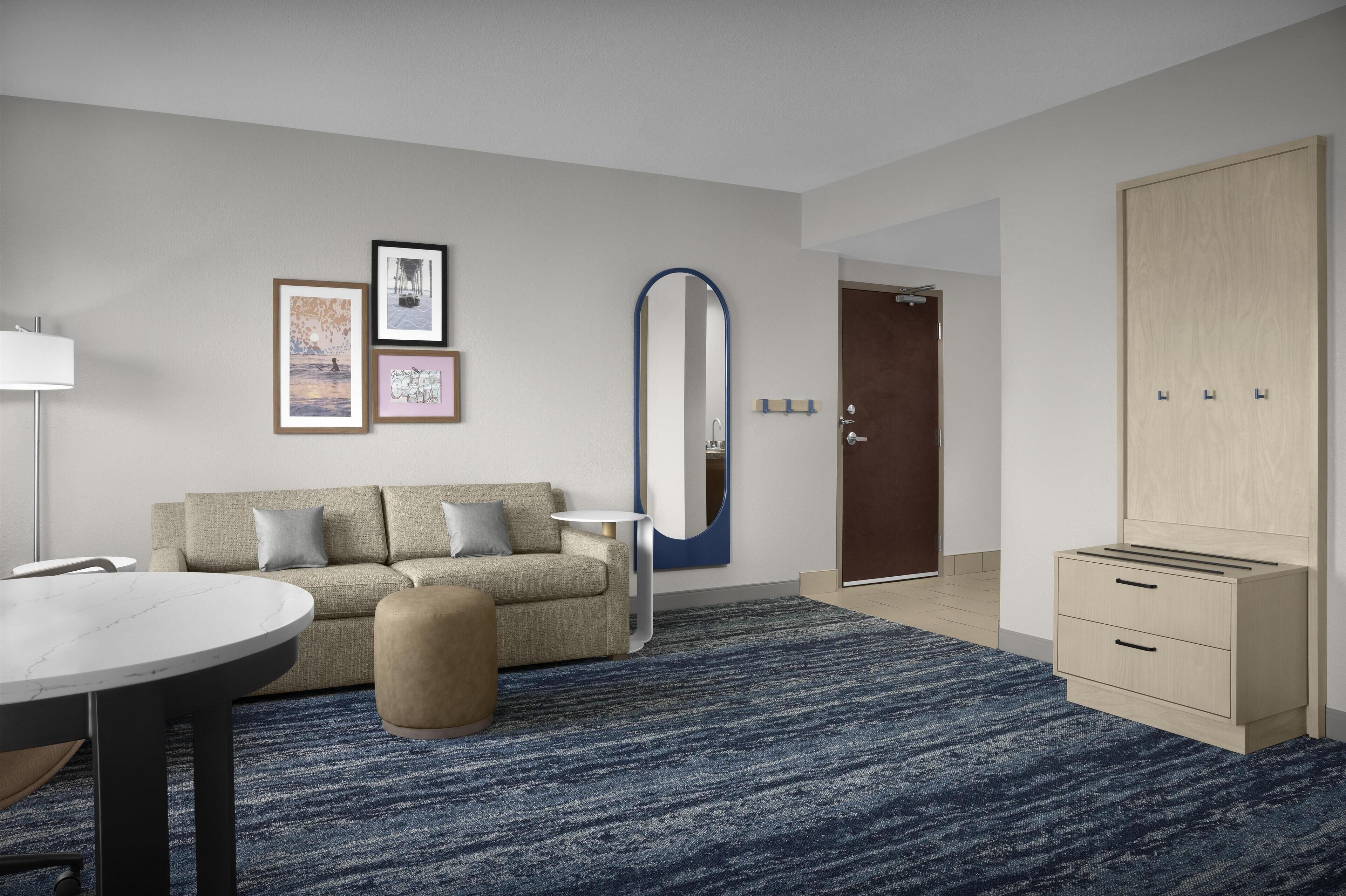 Een moderne hotelkamer met een bank, een ronde tafel, een spiegel en een garderobe.